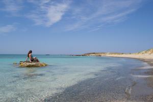a woman sitting on a rock in the water on a beach at Elafonisi Paradise with Parking, WiFi, - Walking Distance to the Beach in Elafonisi