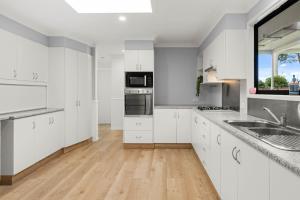 a kitchen with white cabinets and a wooden floor at The 19th Hole by Experience Jervis Bay in Sanctuary Point