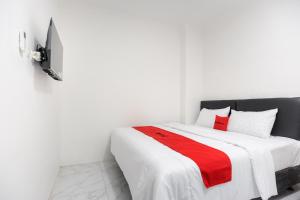 a bedroom with a white bed with a red blanket at RedDoorz Syariah @ Sakura Hotel Jatiwaringin in Bekasi