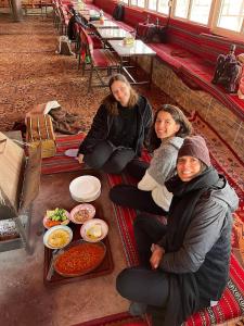 three women sitting on the floor with plates of food at Wadi Rum Backpacker Camp in Wadi Rum