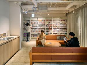 dos personas sentadas en un sofá en una biblioteca en Hotel Plus Hostel TOKYO KAWASAKI, en Kawasaki