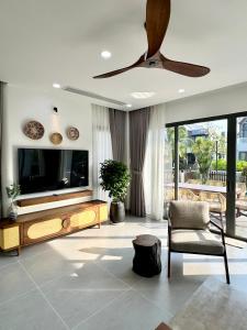 a living room with a tv and a ceiling fan at Tropicana Hồ Tràm - Seashell Villa in Ho Tram