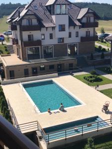 two people sitting in a swimming pool in front of a house at Zlatibor Hills Apartments Wellness & Spa in Zlatibor