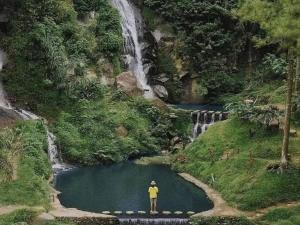 una persona in piedi su un ponte di fronte a una cascata di Villa Estetis di Kota Batu a Malang