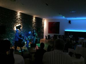 un grupo de personas sentadas en una habitación con un escenario en Hotel Café Schatz, en Hohenems