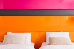 Duas camas com almofadas brancas em frente a uma parede laranja em Hola Hotel Katowice em Katowice