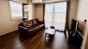 a living room with a leather couch and a television at Apartment Hotel Ecott in Kagoshima