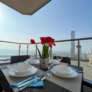 una mesa con platos blancos y flores rojas en el balcón en Almasarat Tower Sea View en Yeda