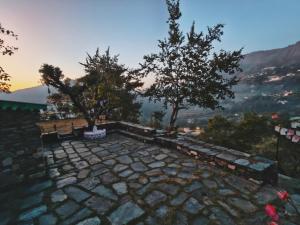 a stone patio with two trees and a bench at Hostel Hideout in Bhīm Tāl