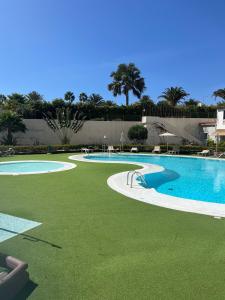 a large swimming pool with green grass next to a building at Lovely apartment Taidia in Maspalomas
