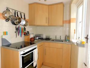 Elle comprend une petite cuisine avec des placards en bois et un évier. dans l'établissement Old Schoolyard Cottage, à Sheringham 10 autres photos