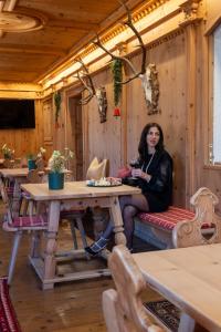 una mujer sentada en una mesa en un restaurante en Belvedere Dolomites Flower Hotel, en Moena