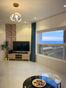 un salon avec une télévision et une grande fenêtre dans l'établissement Jeddah Red Sea View شقة بحرية عصرية, à Djeddah
