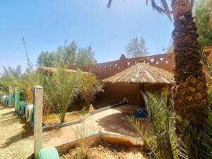 una casa con un ombrello di paglia e una palma di Auberge L'oasis Mhamid a M'Hamid