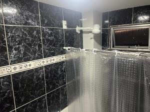 La salle de bains est pourvue d'une douche carrelée de noir avec rideau de douche. dans l'établissement Suite 1, Casa Amarela, Segundo Andar, à Nova Iguaçu
