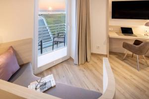 ein Hotelzimmer mit einem Balkon, einem Schreibtisch und einem Bett in der Unterkunft Hotel Stranddistel in Norderney