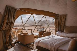 ein Schlafzimmer mit einem Bett und Stühlen sowie einem großen Fenster in der Unterkunft Shaheen Camp Wadi rum in Wadi Rum