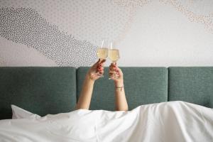 une femme dormant dans un lit tenant des verres de vin dans l'établissement voco Brussels City North, an IHG Hotel, à Vilvorde