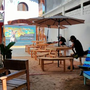 Dois homens sentados em mesas de piquenique debaixo de um guarda-chuva. em Hostal Ledeztrus em Zipolite