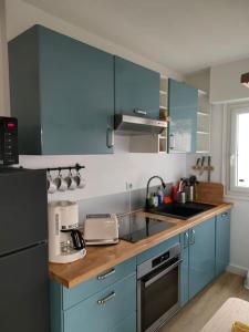 een keuken met blauwe kasten en een wastafel bij Appt RdC terrasse, 300m plage. in Courseulles-sur-Mer