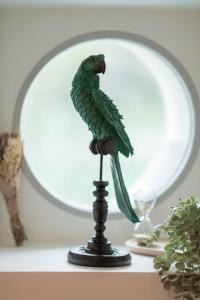 a green parrot on a stand in front of a mirror at Le Logis d'Origine. in Marly-le-Roi