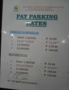 a white menu for pay parking rates on a sign at Sunmiles Condominium in Calamba