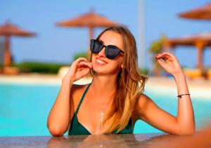 Davinci Beach Hotel في الغردقة: امرأة ترتدي نظارة شمسية تجلس على طاولة بالقرب من مسبح