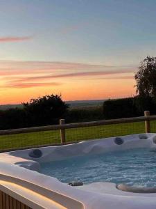 a jacuzzi tub with a sunset in the background at Countryside cottage with private garden & hot tub in Lifton