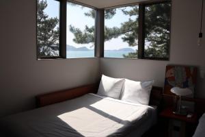 - une chambre avec un lit et 2 fenêtres donnant sur l'océan dans l'établissement Lohas Resort Fukae, à Itoshima