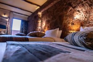 two beds in a room with a stone wall at Hotel Xaluca Dades in Boumalne