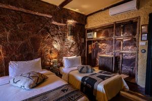 a bedroom with two beds and a stone wall at Hotel Xaluca Dades in Boumalne
