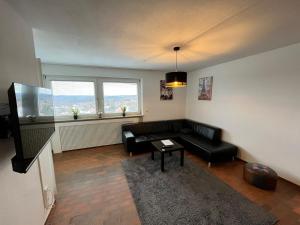 a living room with a black couch and two windows at Premium Apartment 70qm 2,5 Zimmer Küche, Smart TV, Garage, WiFi in Heidenheim an der Brenz