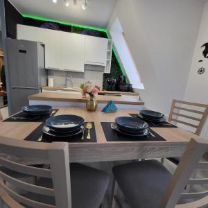 a kitchen with a wooden table with black plates and chairs at PasteLove Studio Apartament Pastelowe blisko Suntago Deepspot Mszczonów in Mszczonów