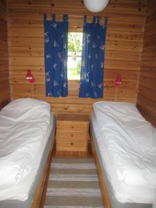 twee bedden in een hut met blauwe gordijnen en een raam bij Ekströms Stugor in Gottby