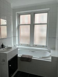 baño con bañera y lavamanos y 2 ventanas en Luxury 3 bedroom, 3 bath apt by Oxford St & Soho, en Londres