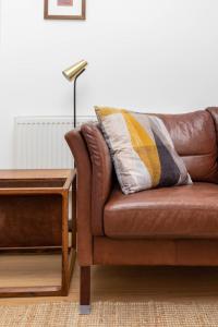 a brown leather couch with a throw pillow and a lamp at Spacious 2BD Flat By Regents Park & Camden Town! in London