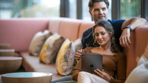 Ein Mann und eine Frau sitzen auf einer Couch mit einem Tablet in der Unterkunft voco Brisbane City Centre, an IHG Hotel in Brisbane