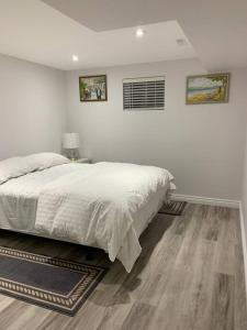 a white bedroom with a bed and a wooden floor at Luxurious brand new ground level apartment in Mississauga
