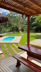 un banco de madera sentado bajo una pérgola junto a una piscina en Sítio Domingos Martins, en Domingos Martins
