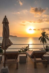 a sunset over the ocean with an umbrella and chairs at Baan Jai Dee Beach Front Hotel in Wok Tum