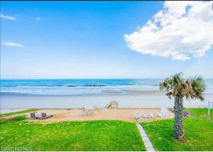 a beach with chairs and a palm tree and the ocean at Freshly Renovated Oceanfront Gem Near St Augustine in Ponte Vedra Beach