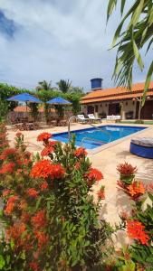 a resort swimming pool with red flowers and blue umbrellas at Belladora Pousada in Barra Grande