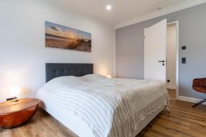 a white bedroom with a bed and a wooden table at Heimathafen an der Eider in Karolinenkoog