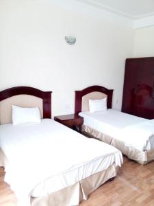 two beds in a room with white walls and wooden floors at Amazon Hotel in Vinh