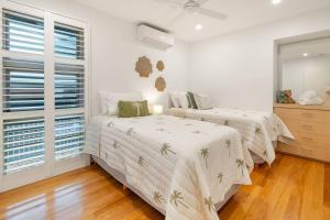 two beds in a bedroom with white walls and wood floors at Luxurious Beachside Living in Mudjimba +14 photos
