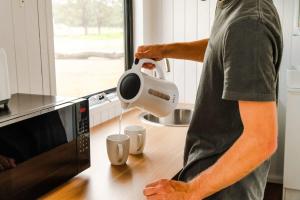a man using a hair dryer in front of a microwave at Odyssean Tiny House in Cessnock