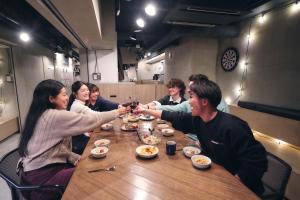 a group of people sitting around a wooden table with food at &AND HOSTEL SHINSAIBASHI EAST in Osaka