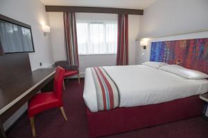 a hotel room with a bed, chair, and a window at Ramada Milton Keynes in Milton Keynes