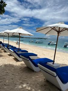 una fila di sedie e ombrelloni blu su una spiaggia di Nusa Indah Bungalow a Nusa Lembongan
