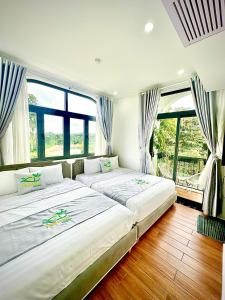 two beds in a room with large windows at Ninh Hoa Garden in Buon Ma Thuot
